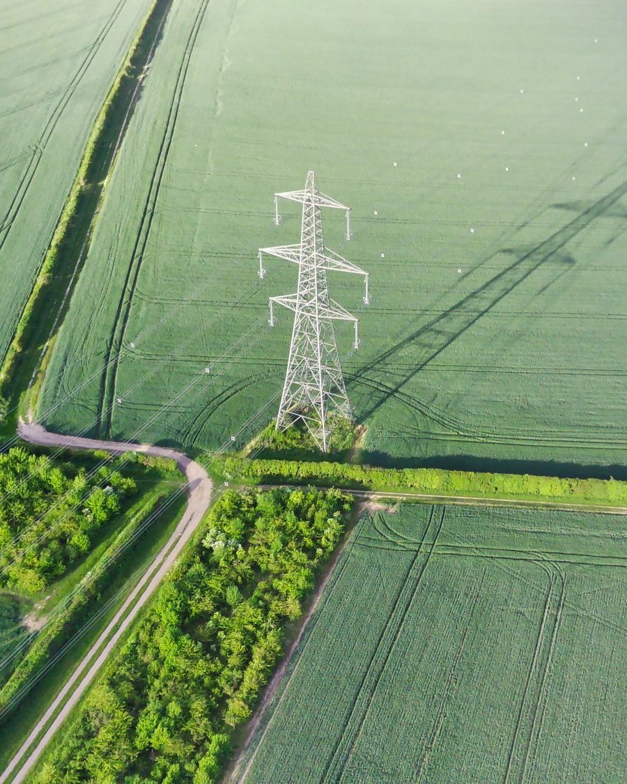 Elektros perdavimo bokštas žaliame lauke iš paukščio skrydžio